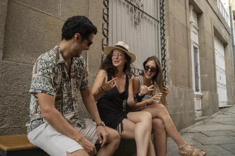 A group of three friends having fun and laughing on a bench in the street Foto stock