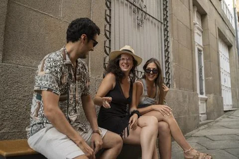 A group of three friends having fun and laughing on a bench in the street Stock Photos