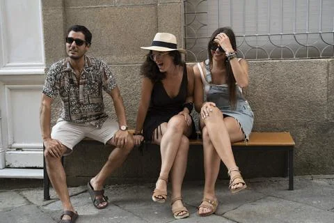 A group of three friends having fun and laughing on a bench in the street Stock Photos