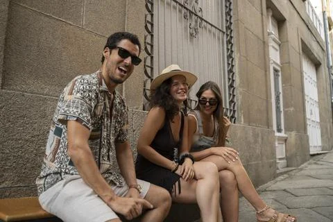 A group of three friends having fun and laughing on a bench in the street Stock Photos