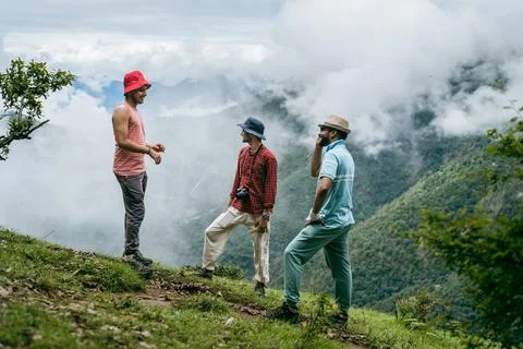 A group of three friends standing on a high altitude grassy meadow ridge talk Stock Photos