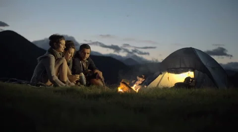 Group of three friends talking, smiling and warming with camp fire in nature Stock Footage 64543793