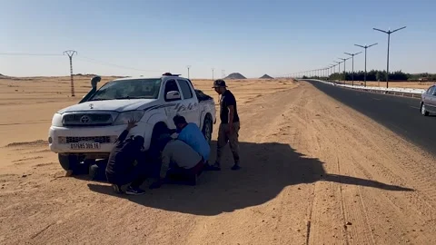 A group of three men working together to change a flat tire on a white Toyota Stock Footage 341899083
