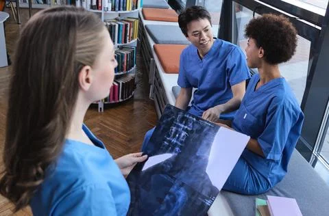Group of three multiracial intern doctors seated in the campus library assess Stock Photos