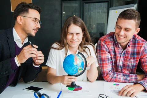 Group of three young people with globe choose country to travel to. Stock Photos