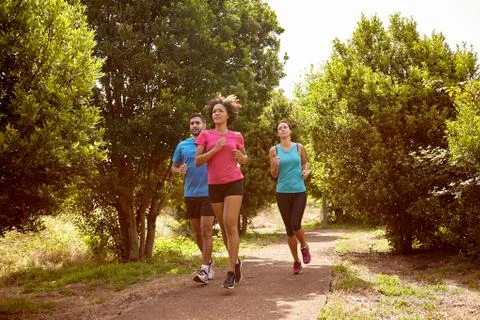 Group of three youngsters running through a natural trail in daylight surroun Stock Photos