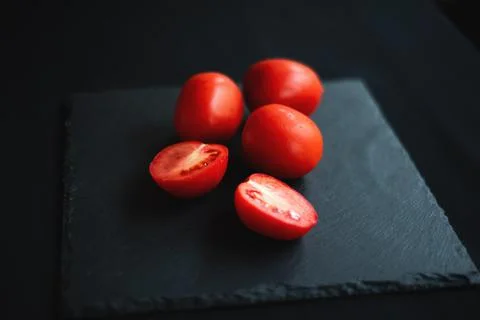 Group of tomatoes, one cut in half, rests on a black board Stock Photos
