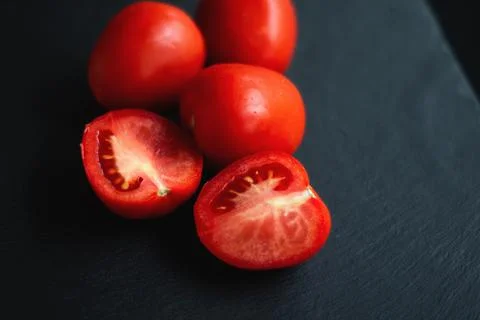 Group of tomatoes, one cut in half, rests on a black board Foto stock