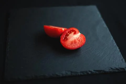 Group of tomatoes, one cut in half, rests on a black board Stock Photos