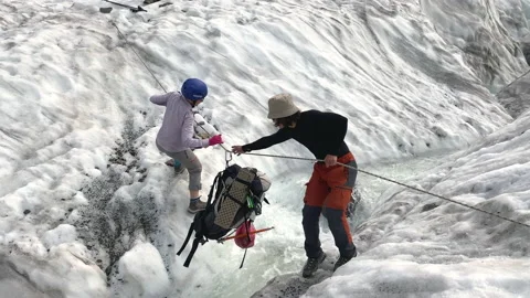 Group of tourists ferries a backpack through a turbulent stream in a glacier Stock Footage 158669734