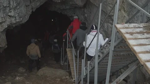 A group of tourists go down the constructed stairs into a wild cave in winter Video stock 169883808
