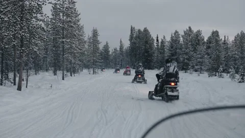 A group of tourists in suits and helmets ride in a convoy on snowmobiles along Stock Footage 158917164