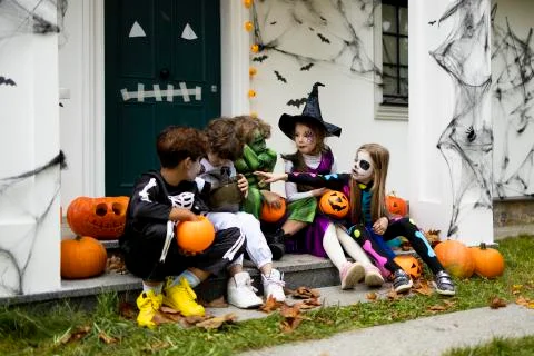 Group of trick-or-treating kids talking and sharing candies on a porch of house Stock Photos