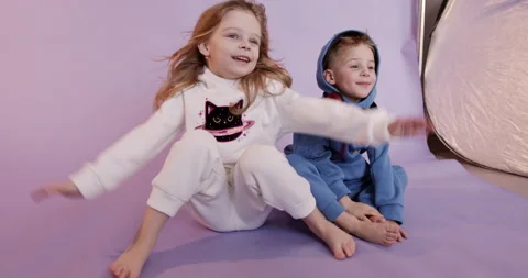 Group of two cheerful children in jumpsuits sitting on floor in studio and Stock Footage 146986797