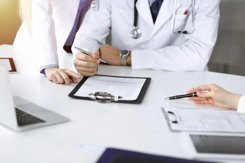Group of unknown doctors are sitting at the desk and discussing problems or Stock Photos