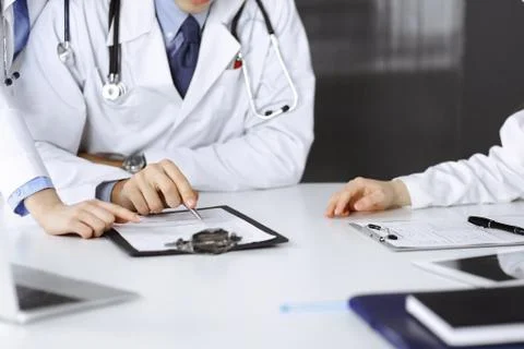 Group of unknown doctors are sitting at the desk and discussing problems or Stock Photos