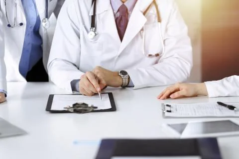 Group of unknown doctors are sitting at the desk and discussing problems or Stock Photos