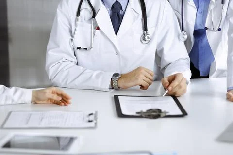 Group of unknown doctors are sitting at the desk and discussing problems or Stock Photos