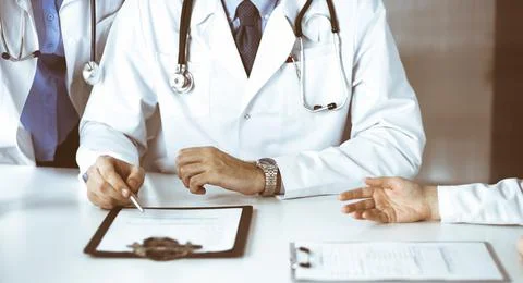 Group of unknown doctors are sitting at the desk and discussing problems or Stock Photos