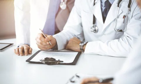 Group of unknown doctors are sitting at the desk and discussing problems or Stock Photos