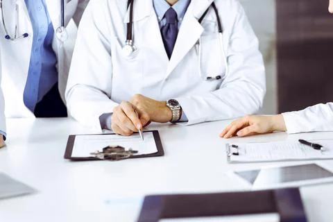 Group of unknown doctors are sitting at the desk and discussing problems or 스톡 사진