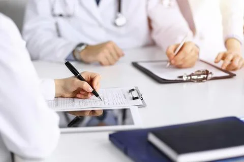 Group of unknown doctors are sitting at the desk and discussing problems or Stock Photos