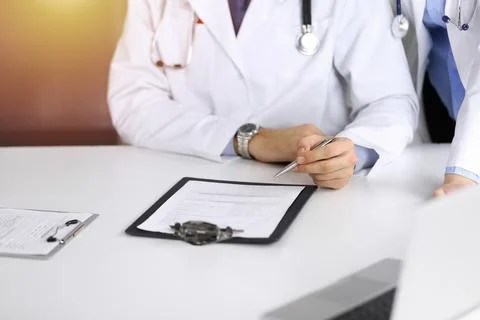 Group of unknown doctors are sitting at the desk and discussing problems or Stockfoto's