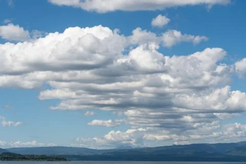 A group of white clouds almost symmetrical between the blue sky and some moun Stock-Fotos