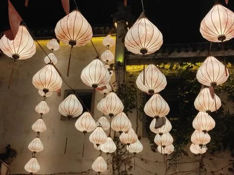 A group of white lanterns with pink patterns hanging on the wall at night ,.. Stock Photos