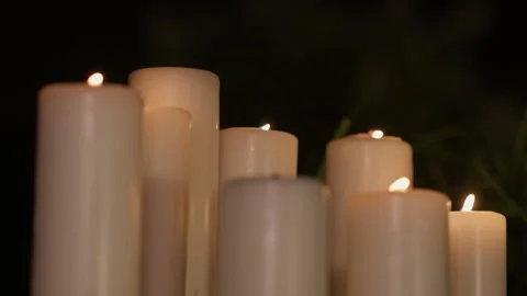 Group of white pillar candles burning against dark background Stock Footage 344512219