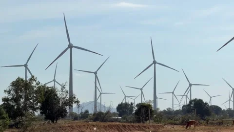 A group of wind generators spins continuously over dry fields, showing active Stock Footage 327908412