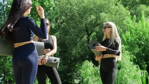 Group of women chats while holding yoga mats, surrounded by lush greenery Stock Footage 333971747