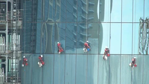 Group of workers cleaning the windows of a high rise building, dangling from Stock Footage 114645430