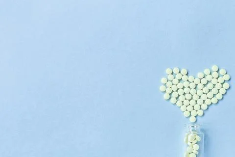 Group of yellow round tablets forms a heart shape on a blue background, spill Stock Photos