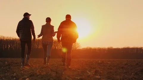 A group of young active farmers is moving forward along a plowed field towards Stock Footage 118643846