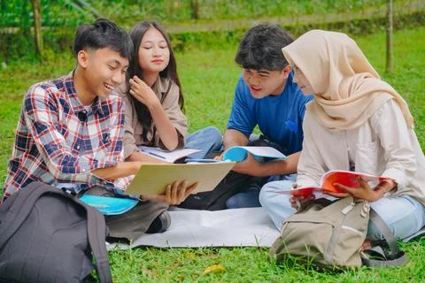 Group of young Asians sit on the grass, concentrating on a piece of paper. Foto stock