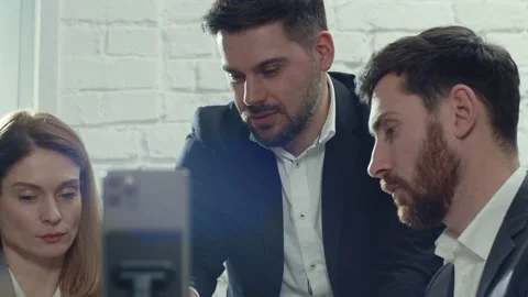 Group of young Caucasian colleagues looking at screen of smartphone, calling Stock Footage