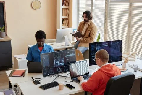 Group of young coworkers analyzing data while sitting in front of computers Stock Photos