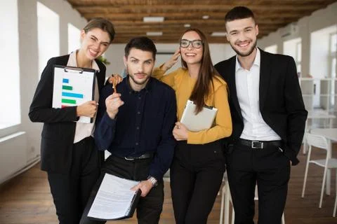 Group of young creative people in suits happily looking in camera together while Stock Photos