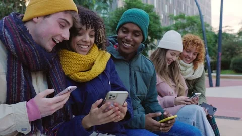 Group of young diverse people using smart phones sitting on bench in winter Stock Footage 303745394