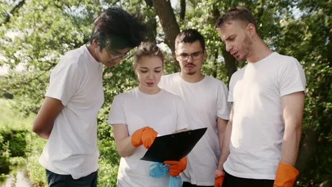 A group of young eco-activists, three guys and a girl, in orange gloves and Stock Footage 223645845