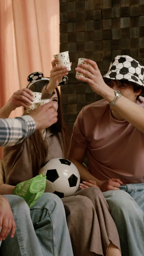 Group of young friends celebrating with drinks and snacks while wearing soccer 库存影片 332678832