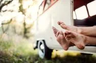 A Group Of Young Friends On A Roadtrip Through Countryside, Feet Sticking Out. Stock Photos