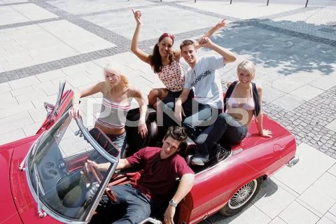 Group Of Young Friends Sitting On Car