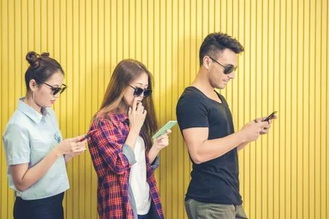 Group of young friends using smart phone against yellow wall ,people addicted by Stock Photos