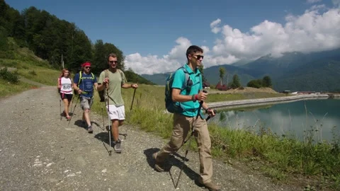 Group of young hikers walks down past transparent blue mountain lake. Instructor Stock Footage 208879823