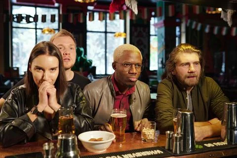 Group of young intercultural friends watching football broadcast together in pub Stock Photos