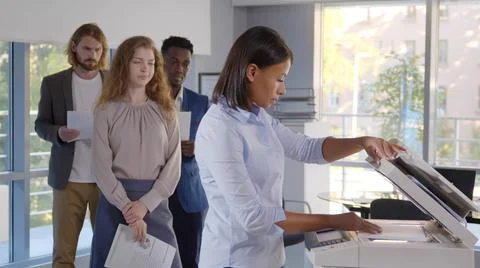Group of young managers standing in queue for copier at office Stock Photos
