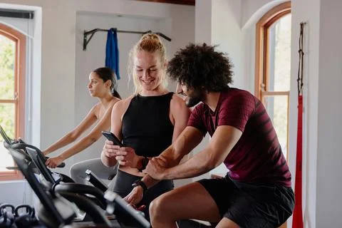 Group of young multiracial friends on exercise bike with mobile phone at the gym Stock Photos