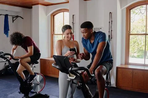 Group of young multiracial friends using mobile phone by exercise bike at the Stock Photos